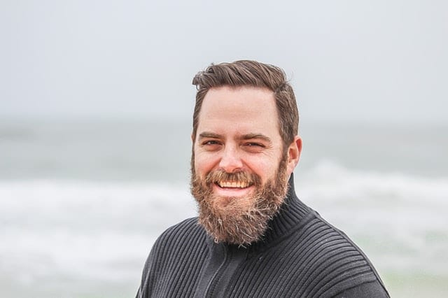 man wearing black zip up jacket near beach smiling at the